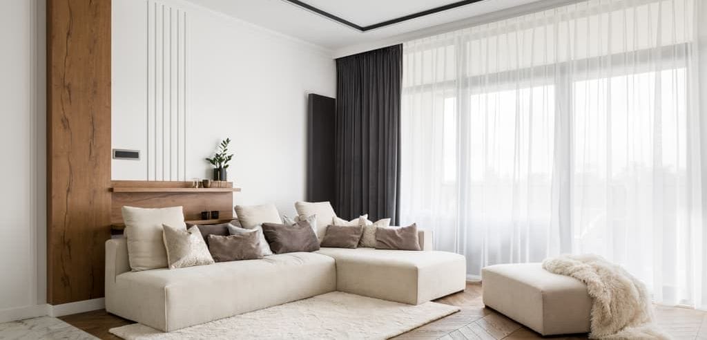 Una sala contemporánea con grandes ventanales que cuentan con cortinas modernas de tela en tonos neutros